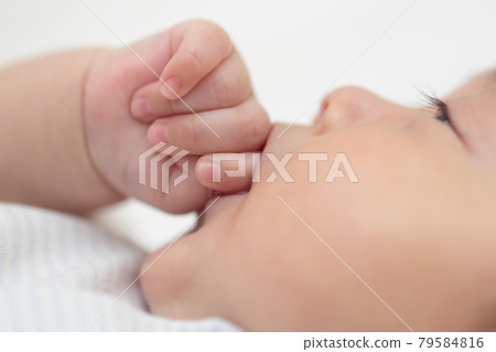 Baby girl lying in bed and sucking fingers 79584816