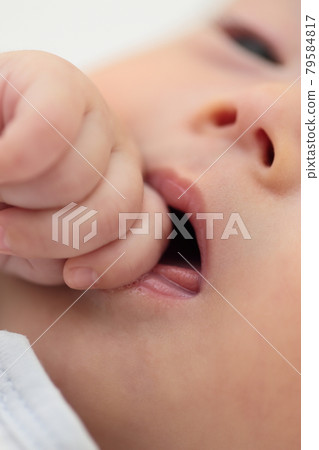 Baby girl lying in bed and sucking fingers 79584817