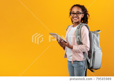 Black girl standing with tablet at yellow studio wall 79585989