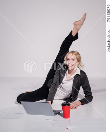 Barefoot ballerina dressed in a business suit poses for a laptop and drinks coffee. Flexible woman works at the computer 79586076