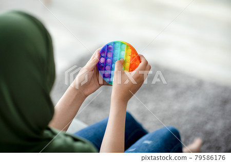 Cropped view of Muslim teenage girl in hijab playing with antistress POP IT toy at home, closeup of hands 79586176