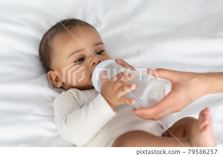 Cute little black baby drinking milk from bottle 79586257