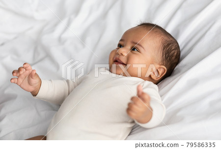 Cute little African American infant lying in bed and laughing Cute little African American infant lying in bed and laughing 79586335