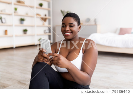 Curvy black lady using mobile device, having break from domestic training, indoors 79586440