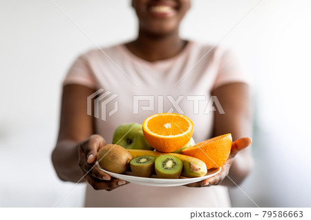 Slimming diet, weight loss and healthy lifestyle. Cropped view of plus size black woman holding plate of fruits indoors Slimming diet, weight loss and healthy lifestyle. Cropped view of plus size black woman holding plate of fruits indoors 79586663