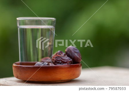 A glass of water and iftar dry dates on plate ready to eat for iftar time. Islamic religion and ramadan concept. Natural blured background with copy space. A glass of water and iftar dry dates on plate ready to eat for iftar time. Islamic religion and ramadan concept. Natural blured background with copy space. 79587033