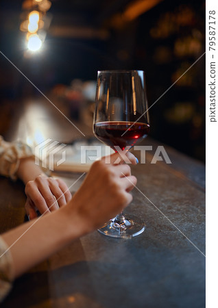 Woman with glass of wine sitting at counter in bar 79587178