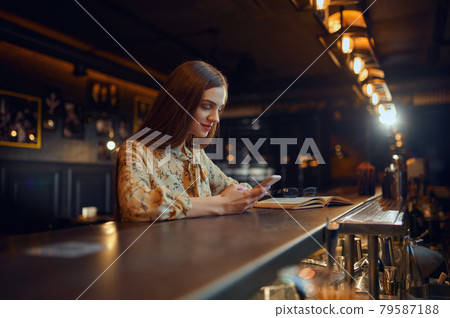 Woman with mobile phone sitting at counter in bar Woman with mobile phone sitting at counter in bar 79587188