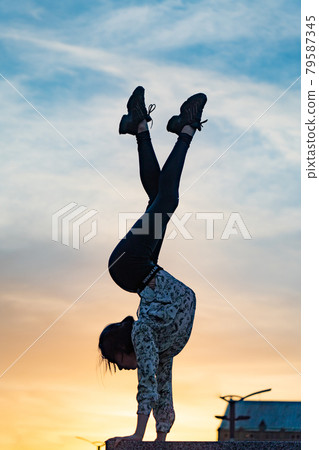 Silhouette of flexible woman gymnast doing handstand on the dramatic sunset. Concept of willpower, motivation and passion Silhouette of flexible woman gymnast doing handstand on the dramatic sunset. Concept of willpower, motivation and passion 79587345