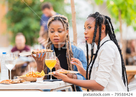 Talking afro american women holding delicious pizza slices: Selective focus Talking afro american women holding delicious pizza slices: Selective focus 79588424