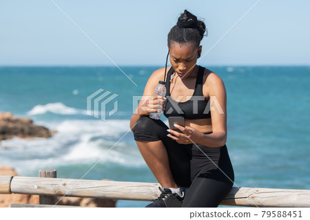 Afro american woman checking her phone on a break after exercising Afro american woman checking her phone on a break after exercising 79588451