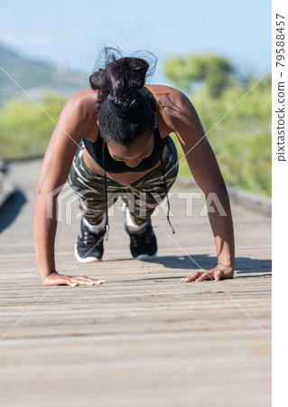 Strong afro american woman doing push ups on a wooden runway: Exercise and healthy lifestyle concept Strong afro american woman doing push ups on a wooden runway: Exercise and healthy lifestyle concept 79588457