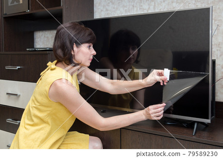 An adult brunette woman with a rainbow removes a protective film from a new lcd TV screen An adult brunette woman with a rainbow removes a protective film from a new lcd TV screen 79589230