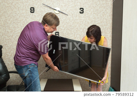 A man and a woman bring a new TV into the apartment 79589312