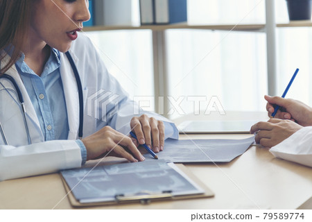 Two asian women doctors discuss meeting doctor's office medical clinic looking x-ray film consulting patient disease. Asian medical lab young women talking together discussing healthcare teamwork Two asian women doctors discuss meeting doctor's office medical clinic looking x-ray film consulting patient disease. Asian medical lab young women talking together discussing healthcare teamwork 79589774