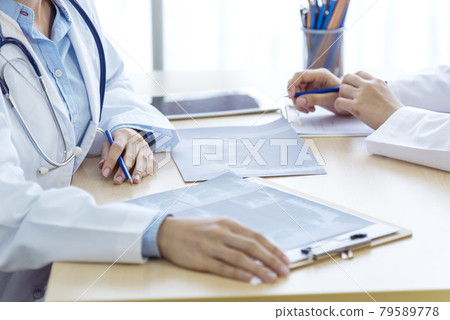 Two asian women doctors discuss meeting doctor's office medical clinic looking x-ray film consulting patient disease. Asian medical lab young women talking together discussing healthcare teamwork Two asian women doctors discuss meeting doctor's office medical clinic looking x-ray film consulting patient disease. Asian medical lab young women talking together discussing healthcare teamwork 79589778