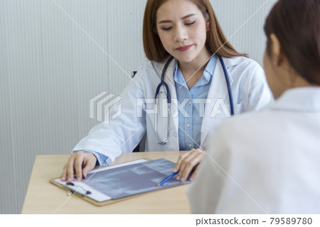 Two asian women doctors discuss meeting doctor's office medical clinic looking x-ray film consulting patient disease. Asian medical lab young women talking together discussing healthcare teamwork 79589780