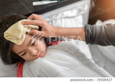 Asian mother take cool towel for reduce high fever on sick girl forehead on bed at morning time, Selective focus, Healthy and infection concept Asian mother take cool towel for reduce high fever on sick girl forehead on bed at morning time, Selective focus, Healthy and infection concept 79590427