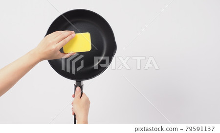 Pan cleaning. Man hand on white background cleaning the non stick pan with handy dish washing sponge which yellow color on the soft side and green on hard side for hygiene after cook. Electric pan. Pan cleaning. Man hand on white background cleaning the non stick pan with handy dish washing sponge which yellow color on the soft side and green on hard side for hygiene after cook. Electric pan. 79591137