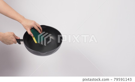 Pan cleaning. Man hand on white background cleaning the non stick pan with handy dish washing sponge which yellow color on the soft side and green on hard side for hygiene after cook. Electric pan. Pan cleaning. Man hand on white background cleaning the non stick pan with handy dish washing sponge which yellow color on the soft side and green on hard side for hygiene after cook. Electric pan. 79591143