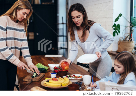 Young women set the table, girl does her homework Young women set the table, girl does her homework 79592762