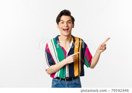 Happy gay man laughing and smiling, pointing fingers right at promo offer, standing over white background Happy gay man laughing and smiling, pointing fingers right at promo offer, standing over white background 79592846