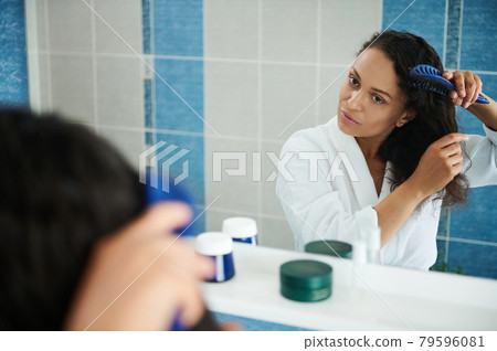 Attractive woman looking at her mirror reflection while combing hait in bathroom 79596081
