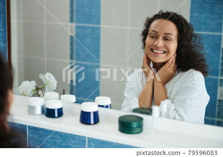 Middle aged African-American woman cute smiles looking at her reflection in the bathroom mirror Middle aged African-American woman cute smiles looking at her reflection in the bathroom mirror 79596083