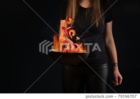 Shrimp tails and vegetables hovering in fire over wok pan in female hands 79596707
