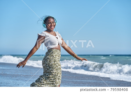 young african american woman listening to music by the shore of the beach 79598408