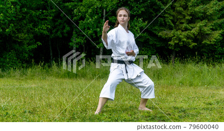 teenage girl training karate kata outdoors, performs soto uke or outside block in kakutsu dachi stand teenage girl training karate kata outdoors, performs soto uke or outside block in kakutsu dachi stand 79600040