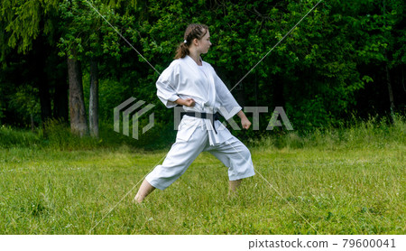 teenage girl training karate kata outdoors, performs gedan-barai or downward block 79600041