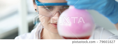 Woman researcher in glasses is conducting chemical experiment in flask Woman researcher in glasses is conducting chemical experiment in flask 79601827