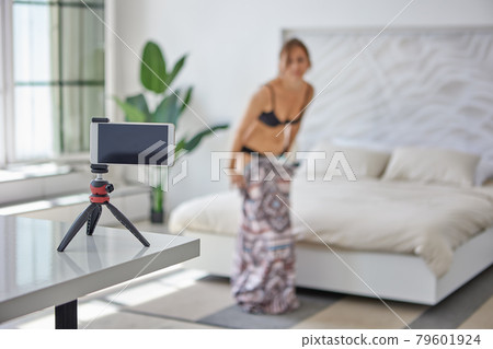 Young woman undresses in front of smartphone camera, defocused image, selective focus. Young woman undresses in front of smartphone camera, defocused image, selective focus. 79601924