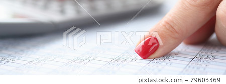 Woman pointing her index finger at numbers in table and counting on calculator closeup 79603369