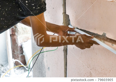 Electrician concealing electicity power wire lines within plastic tube embeded into wall Electrician concealing electicity power wire lines within plastic tube embeded into wall 79603905