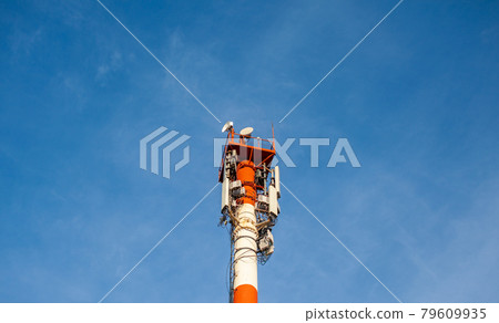 A white and red tower with cellular communication antennas on a sky 79609935