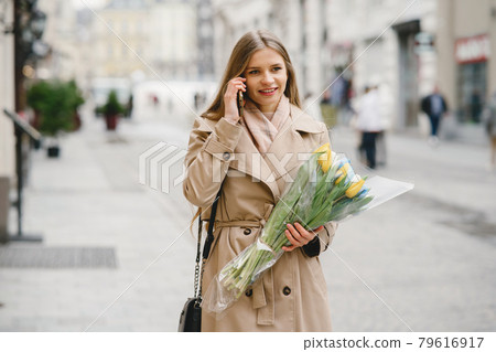 Elegant blonde standing on the street with flowers Elegant blonde standing on the street with flowers 79616917
