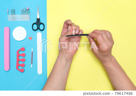 Woman files her nails. Gives himself a manicure. Elderly hands. Yellow-blue background. Beauty concept. Woman Hand Care Woman files her nails. Gives himself a manicure. Elderly hands. Yellow-blue background. Beauty concept. Woman Hand Care 79617486