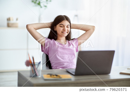 Joyful Indian teen girl holding hands behind head, relaxing in front of laptop at home 79620371