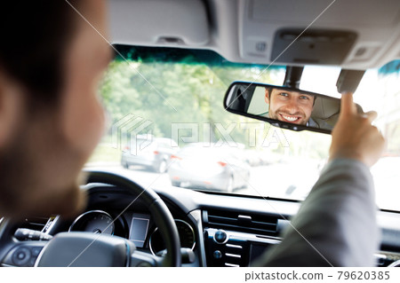 Millennial caucasian guy in suit with hands on steering wheel, configures mirror 79620385