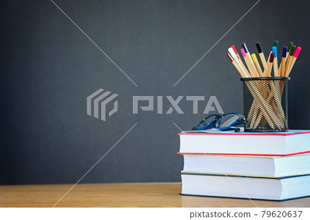 A stack of books, glasses, many pencils in the metal holder on the wooden background of a black school board. The concept of education. Copy blank space.Template 79620637