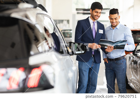 Middle-eastern guy having conversation with sales assistant in auto showroom Middle-eastern guy having conversation with sales assistant in auto showroom 79620751