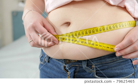 Closeup of young woman loosing weight measuring her waist. Concept of dieting, unhealthy lifestyle, overweight and obesity Closeup of young woman loosing weight measuring her waist. Concept of dieting, unhealthy lifestyle, overweight and obesity 79625465