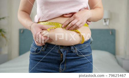 Young woman thinking of loosing weight measuring her waist with measuring tape. Concept of dieting, unhealthy lifestyle, overweight and obesity Young woman thinking of loosing weight measuring her waist with measuring tape. Concept of dieting, unhealthy lifestyle, overweight and obesity 79625467