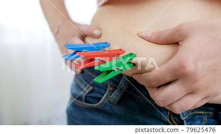 Young woman loosing weight hanging clothespins on her big belly. Concept of excessive weight, obese female, dieting and overweight problems Young woman loosing weight hanging clothespins on her big belly. Concept of excessive weight, obese female, dieting and overweight problems 79625476