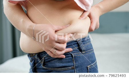 Young overweight woman looking in mirror and touching her fat belly. Concept of excessive weight, obese female, dieting and overweight problems 79625493