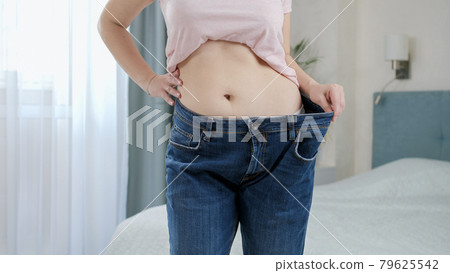 Beautiful slim woman wearing her old jeans that are big for her. Concept of dieting, loosing weight and healthy lifestyle. Beautiful slim woman wearing her old jeans that are big for her. Concept of dieting, loosing weight and healthy lifestyle. 79625542