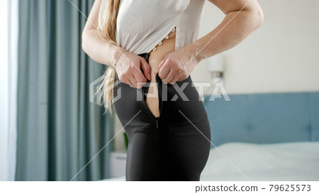 Young woman struggling to xip up tight dress. Concept of excessive weight, obese female, dieting and overweight problems Young woman struggling to xip up tight dress. Concept of excessive weight, obese female, dieting and overweight problems 79625573
