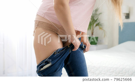 CLoseup of young woman with belly struggling to dress in tight jeans and button them. Concept of excessive weight, obese female, dieting and overweight problems 79625666